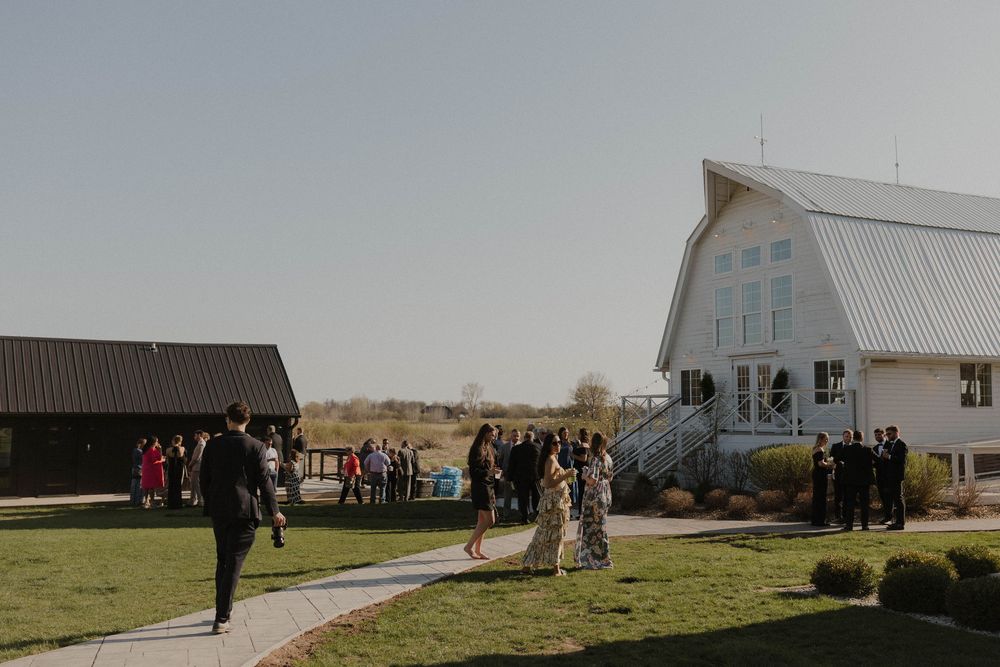 Panoramic view of a white chapel and barn venue in a rural setting under blue sky.