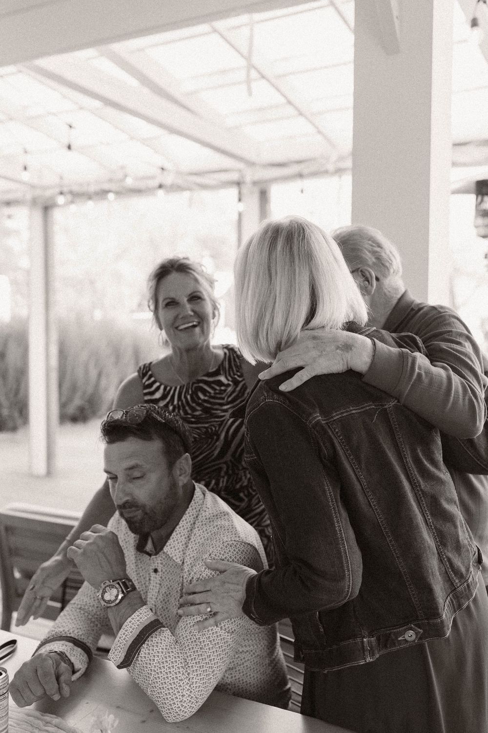 Candid black and white photo of guests laughing and embracing at a celebration.