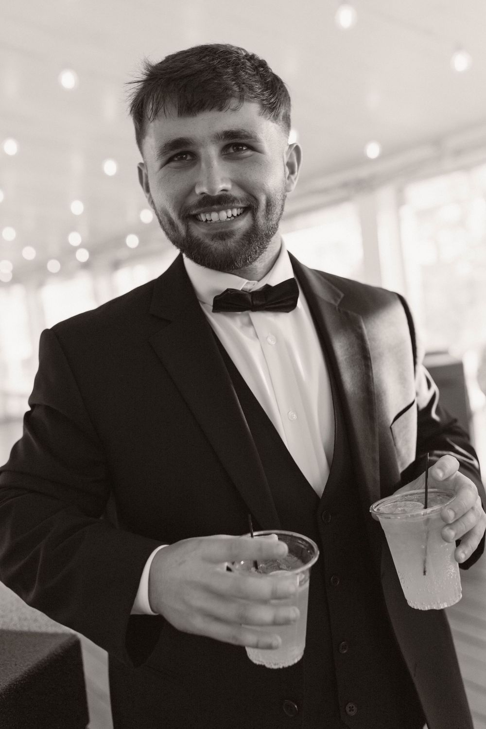 Wedding guest in black suit and bowtie enjoys cocktails at an elegant reception.