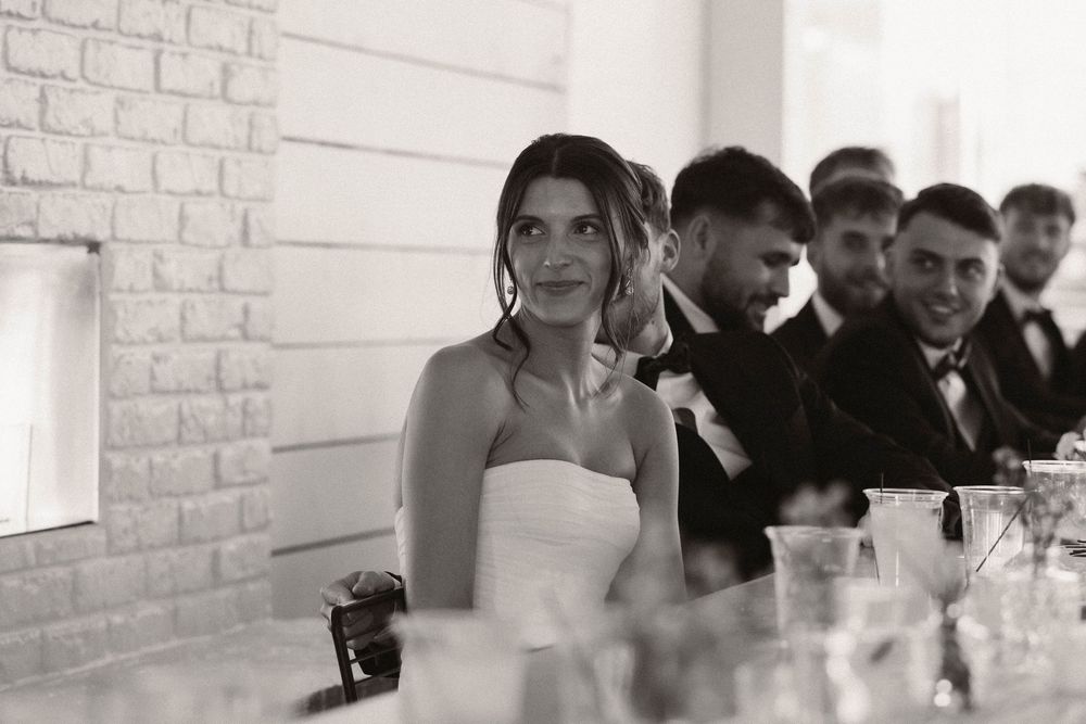 Wedding guests seated at long tables in a bright white reception venue with brick walls.