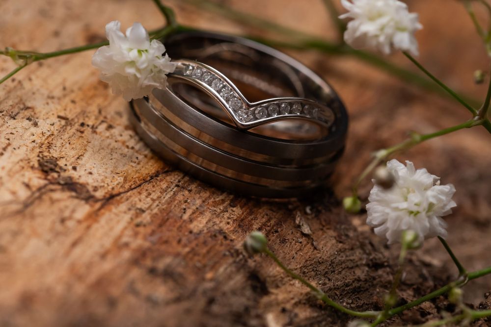 Wedding rings photographed with delicate white flowers on wooden surface.