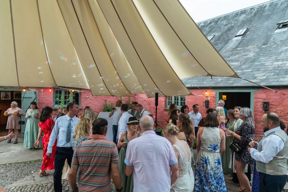Wedding guests mingling under a large outdoor tent or marquee.