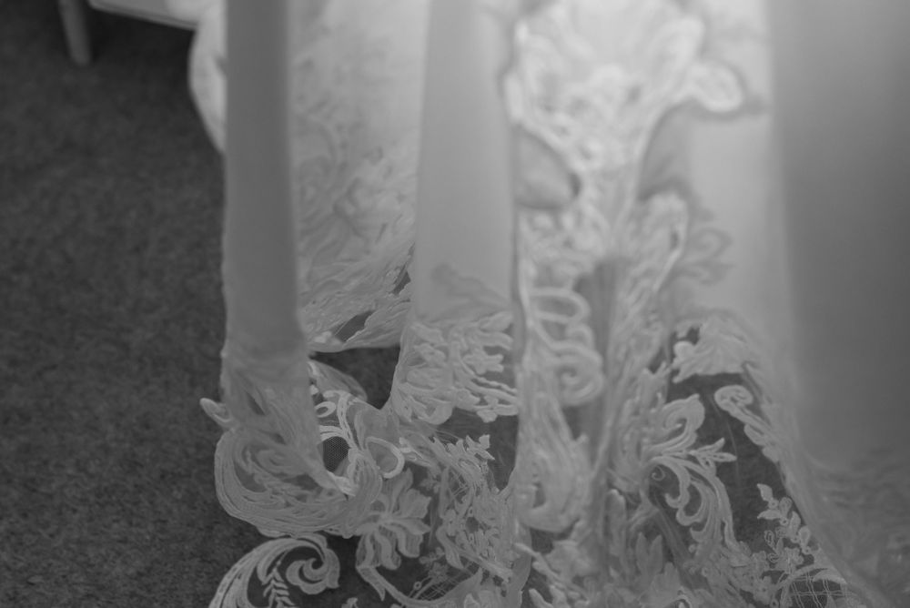 Close-up details of white lace wedding dress against light background.