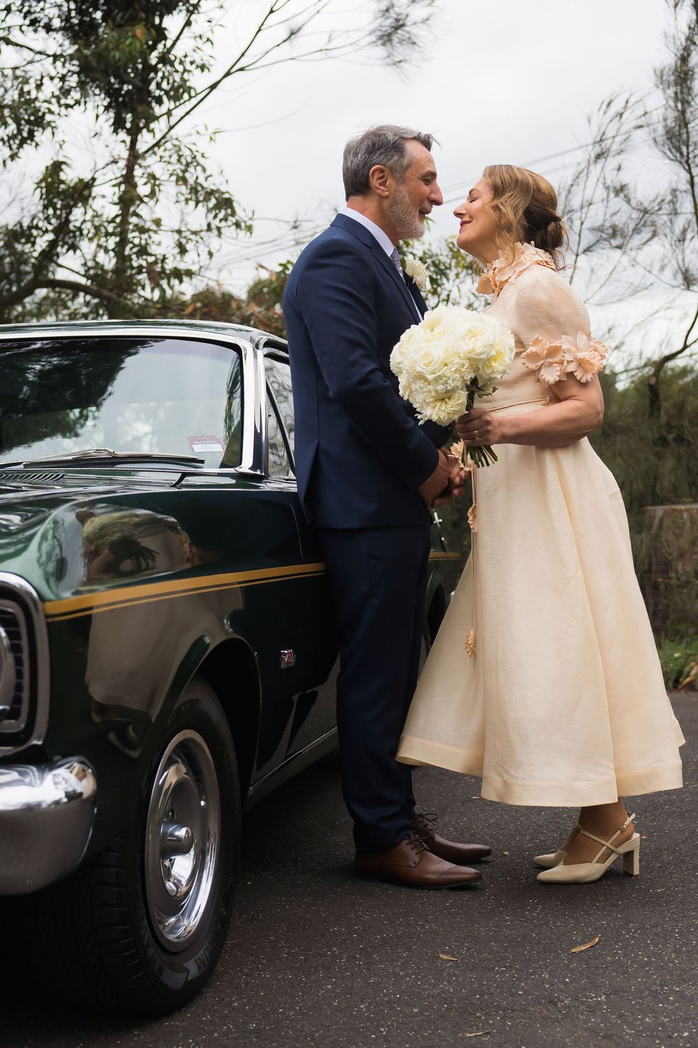 A classic black vintage car serves as a romantic backdrop for newlyweds sharing a tender moment together.