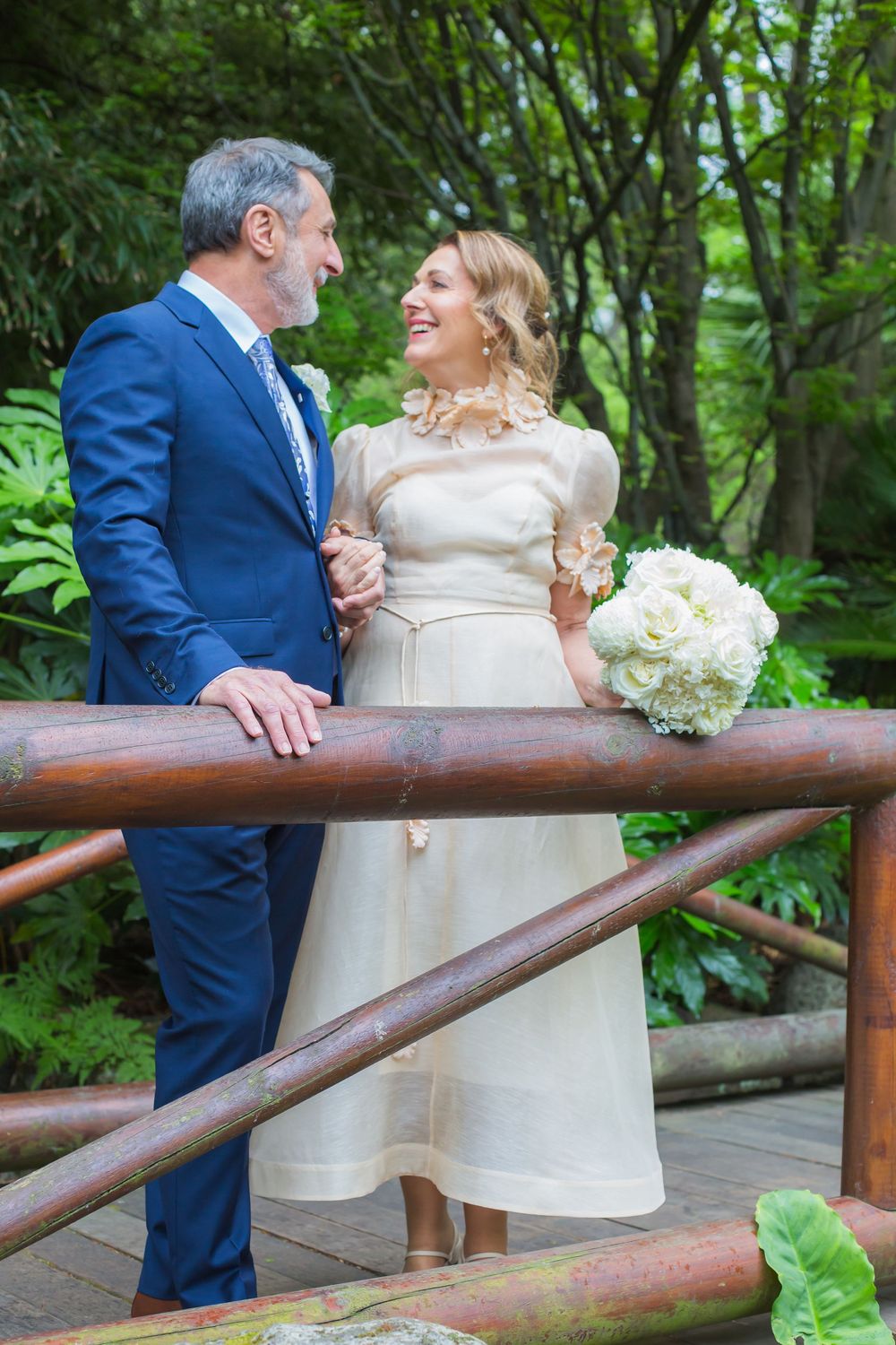 A couple shares a joyful moment on a rustic wooden bridge surrounded by lush greenery in a garden setting.