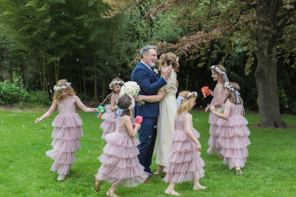 Wedding party poses on green lawn wearing pink ruffled dresses and formal attire during outdoor celebration.