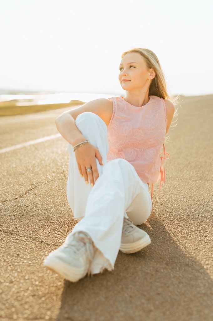 Person in casual attire sits cross-legged on asphalt during golden hour sunset, creating a dreamy atmospheric mood.