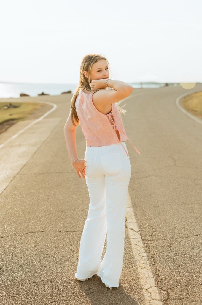 Someone in pink top and white pants walks on a winding country road at sunset.