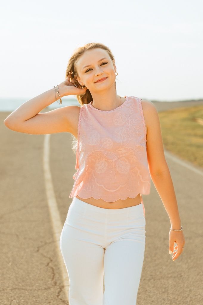 A person in a pink lace crop top and white pants poses elegantly against a sunlit outdoor landscape.