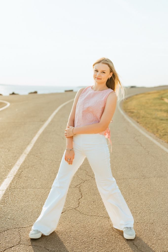 Person in white pants and pink top poses playfully in sequence along an empty rural road during golden hour.