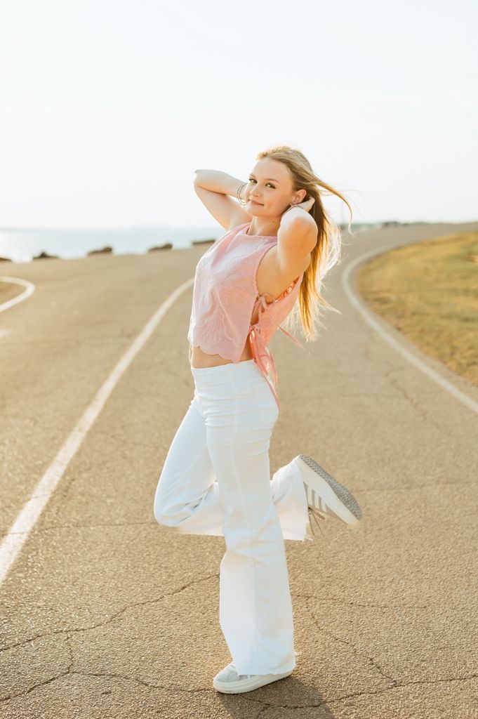 A figure in white pants and pink shirt dances playfully on a winding dirt road through golden hills.