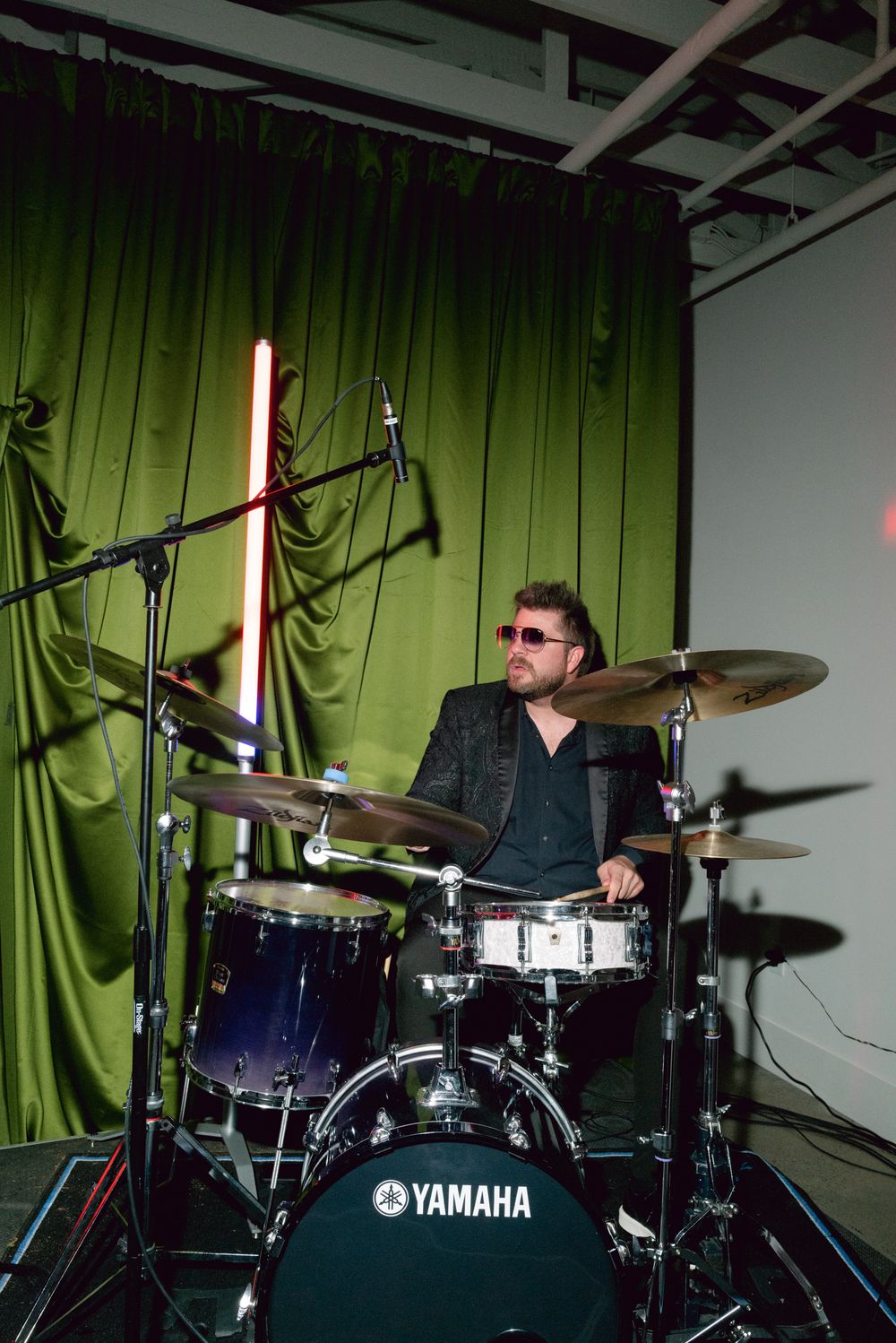 Drummer performing energetically on a Yamaha drum kit against a green curtain backdrop in sequence of action shots.