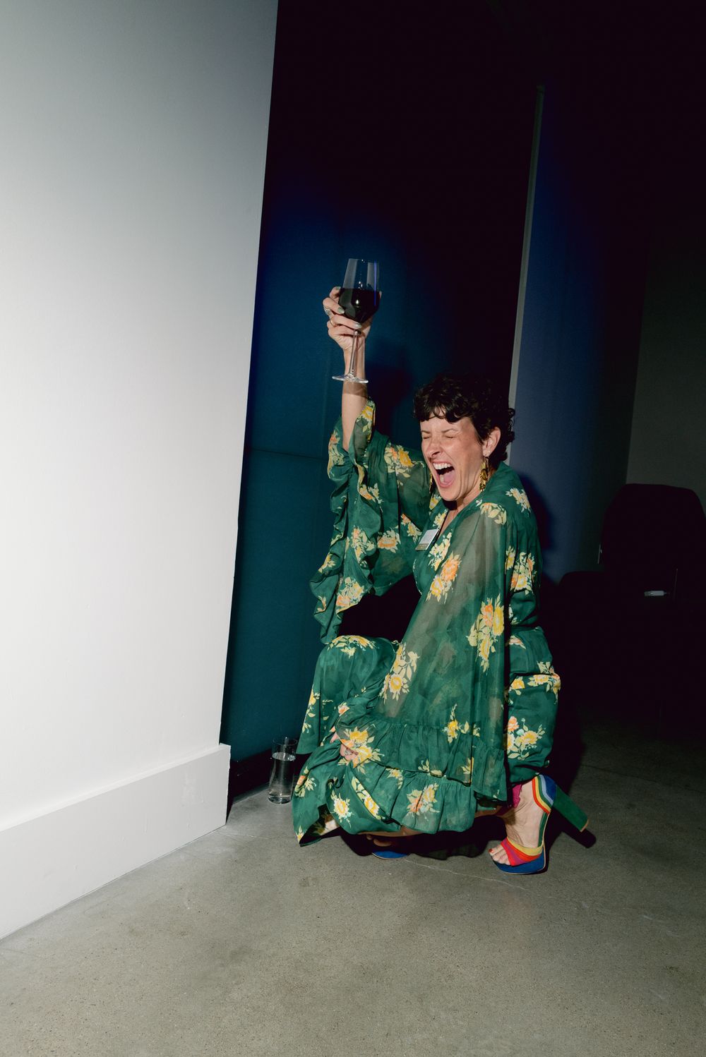 Someone in a green and gold patterned coat performs expressively on the floor against a dark background.