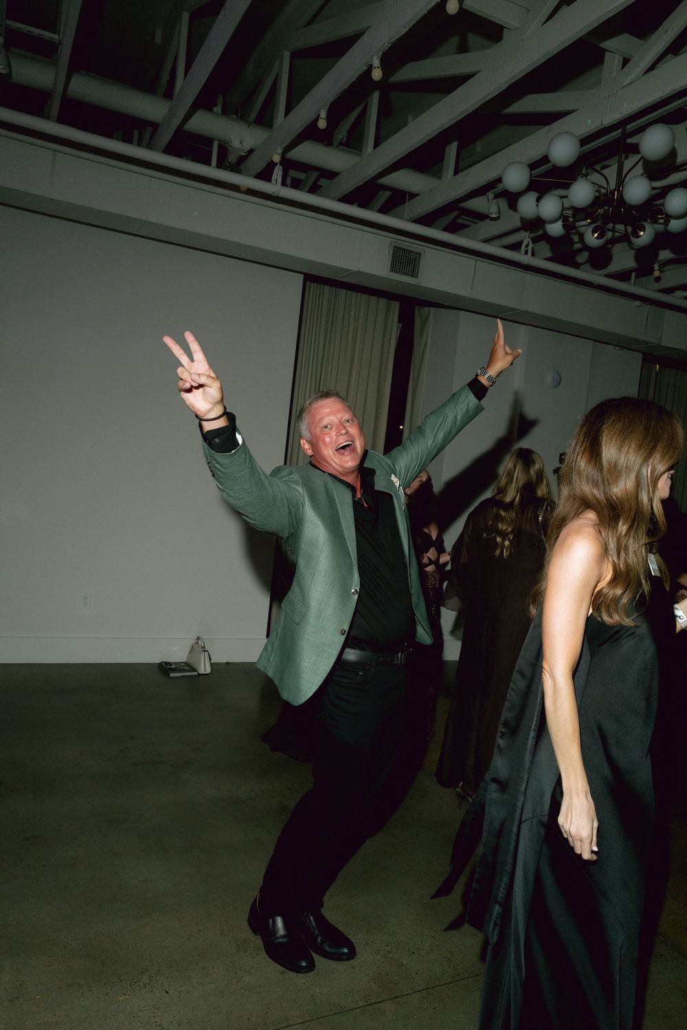 People dancing enthusiastically in a dimly lit space with industrial ceiling beams visible above.