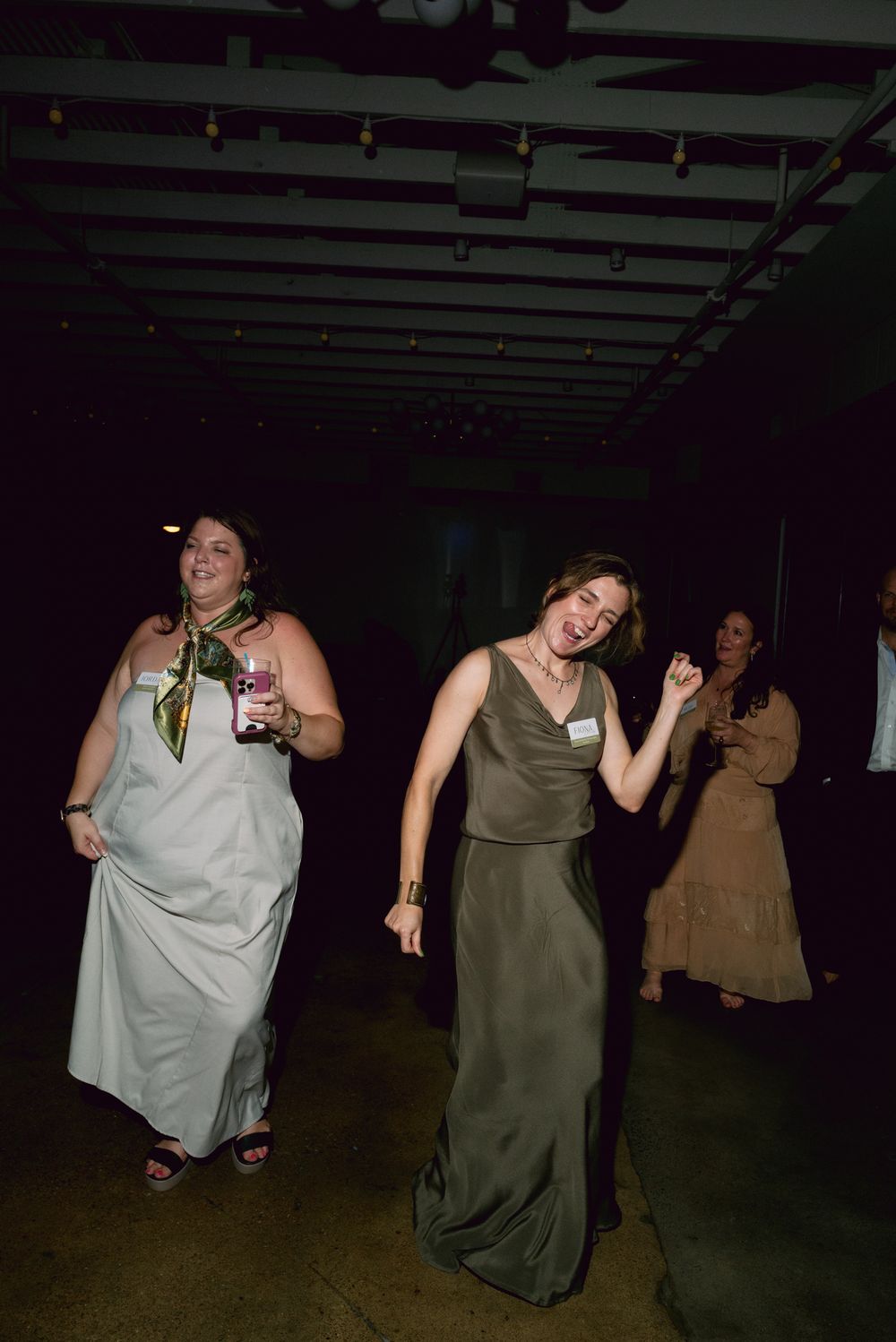 People dancing and having fun at a party in dresses at a dimly lit indoor venue.