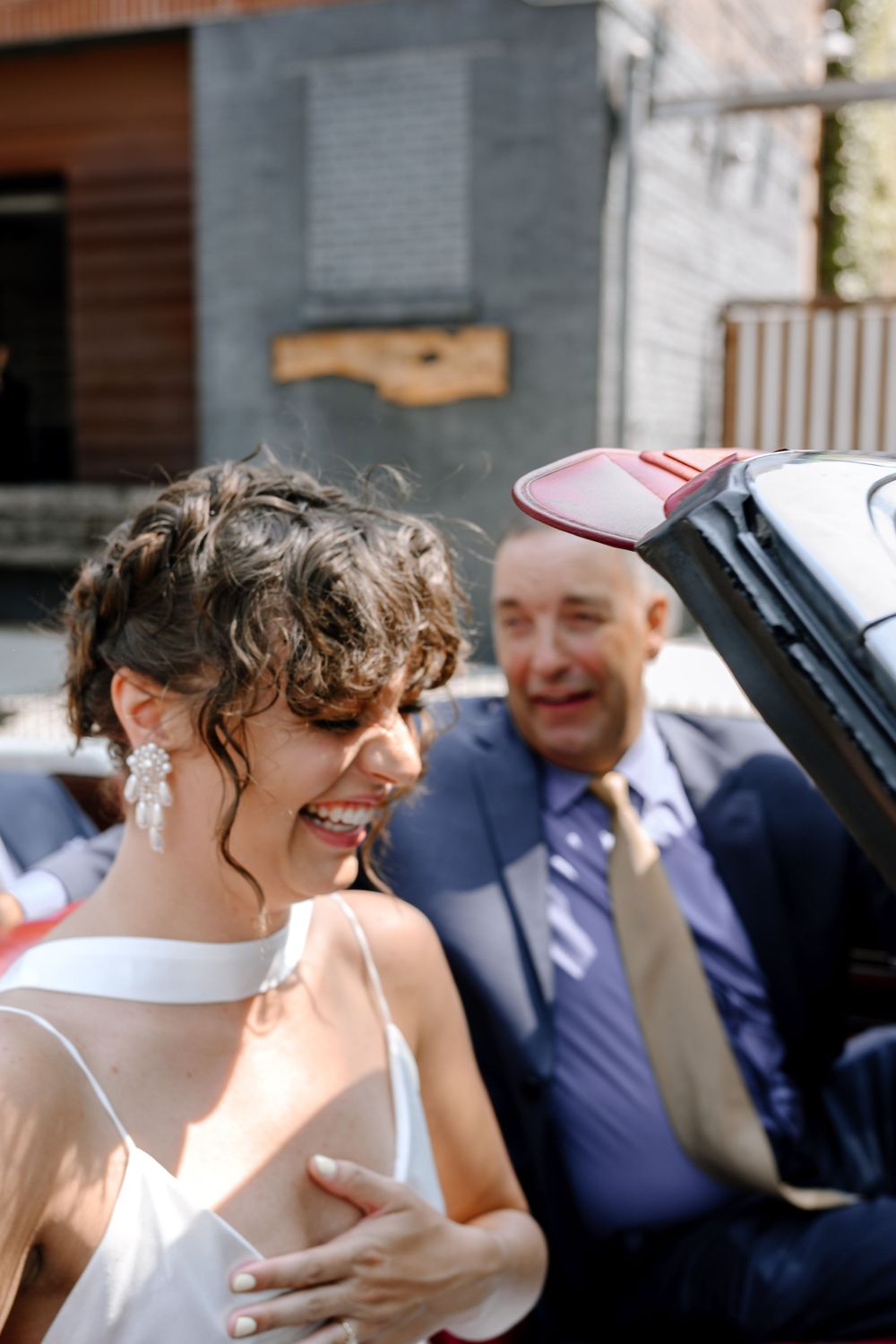A joyous outdoor wedding moment captured in natural sunlight, featuring a bride with curly hair in a white dress.