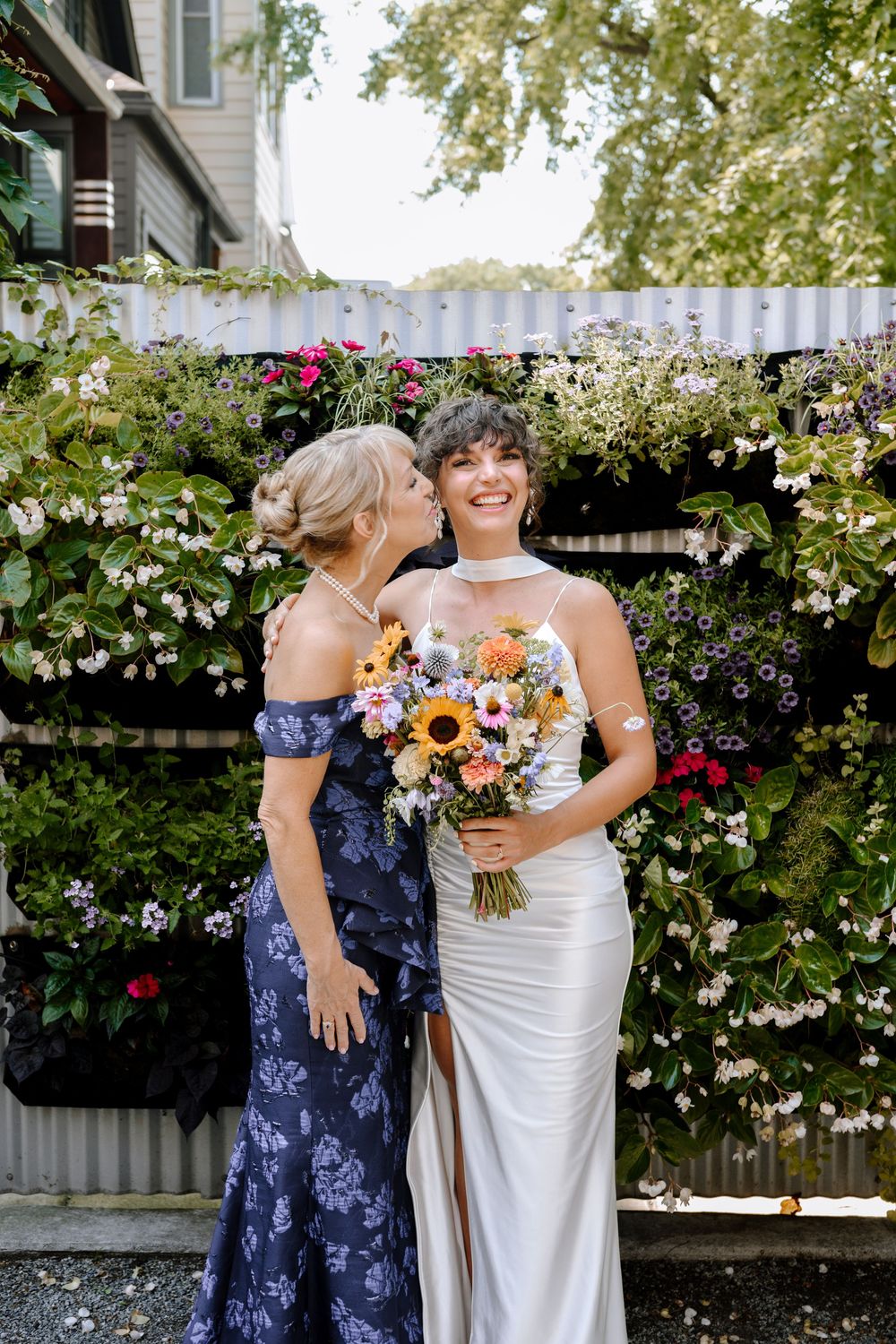 Wedding party with bouquets posing in garden setting with white roses and sunflowers.