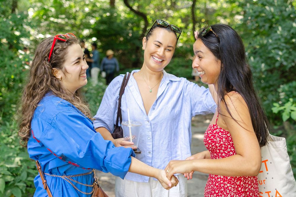 Three women greet each other and smile together in Central Park after the woman in red gets engaged in August.