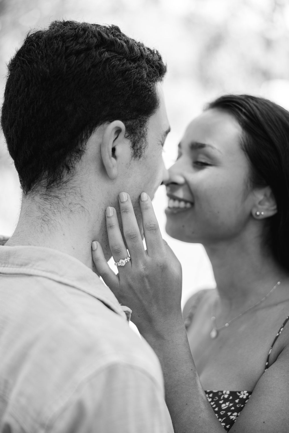 A romantic black and white engagement photo shows a couple sharing an intimate moment as she displays her ring in Central Park.