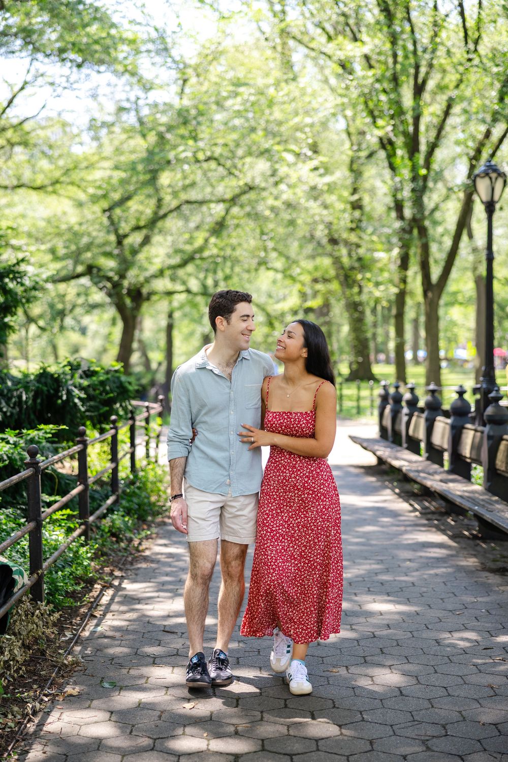 Couple walks together on brick path through lush green park on sunny summer day in New York City.