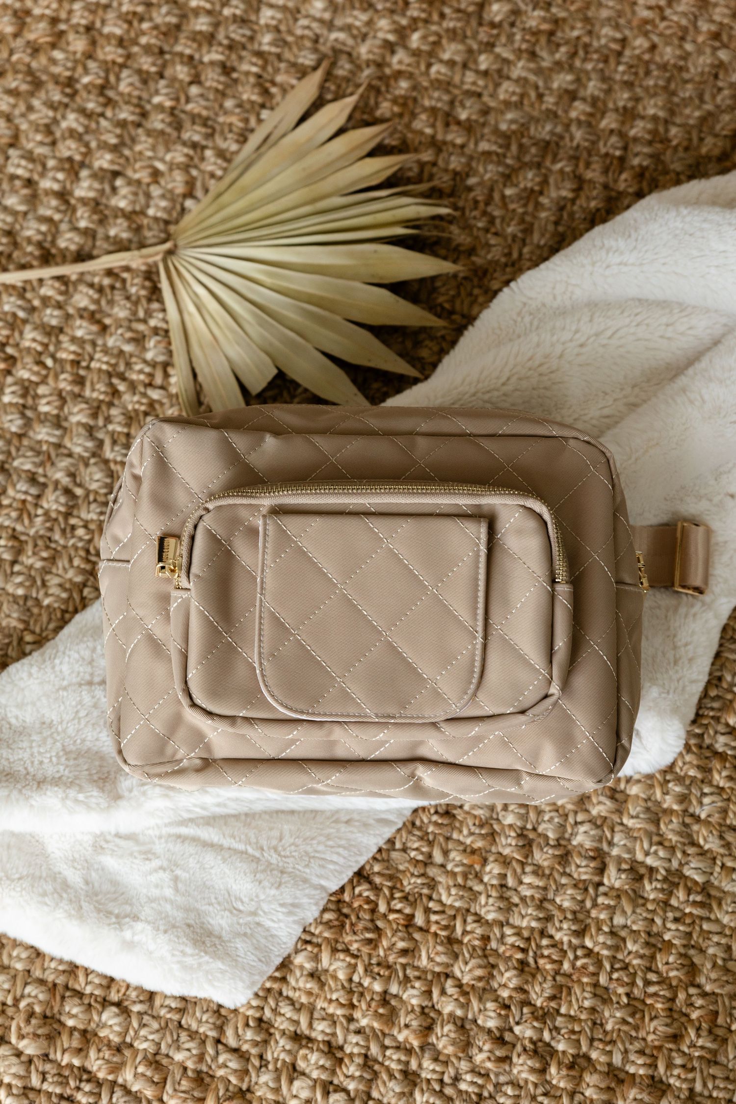khaki diaper bag with a big palm leaf as decor next to it