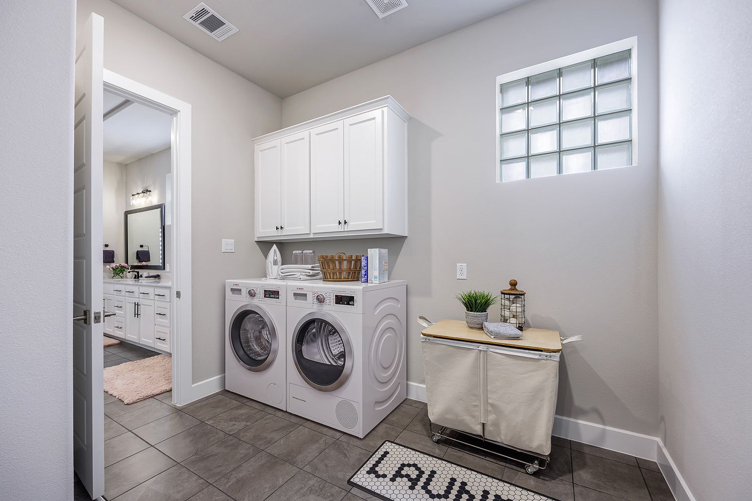Modern laundry room features side-by-side washer and dryer with white subway tile backsplash and storage cabinets.