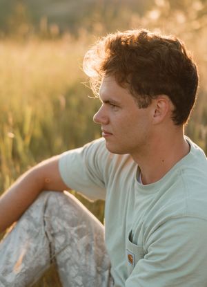 Profile portrait of someone sitting outdoors in a light blue t-shirt during golden hour sunset lighting in a grassy field.