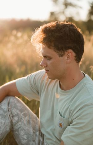 Profile portrait in soft golden sunlight of someone wearing a white Carhartt pocket t-shirt sitting outdoors.