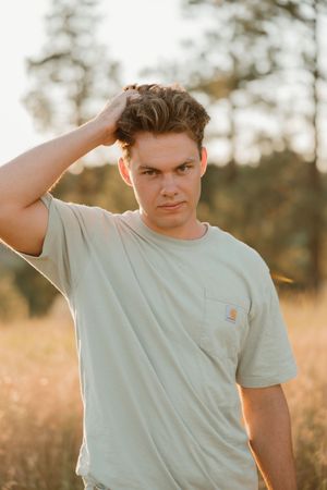 Young person in light blue t-shirt poses outdoors in a grassy field during golden hour lighting.