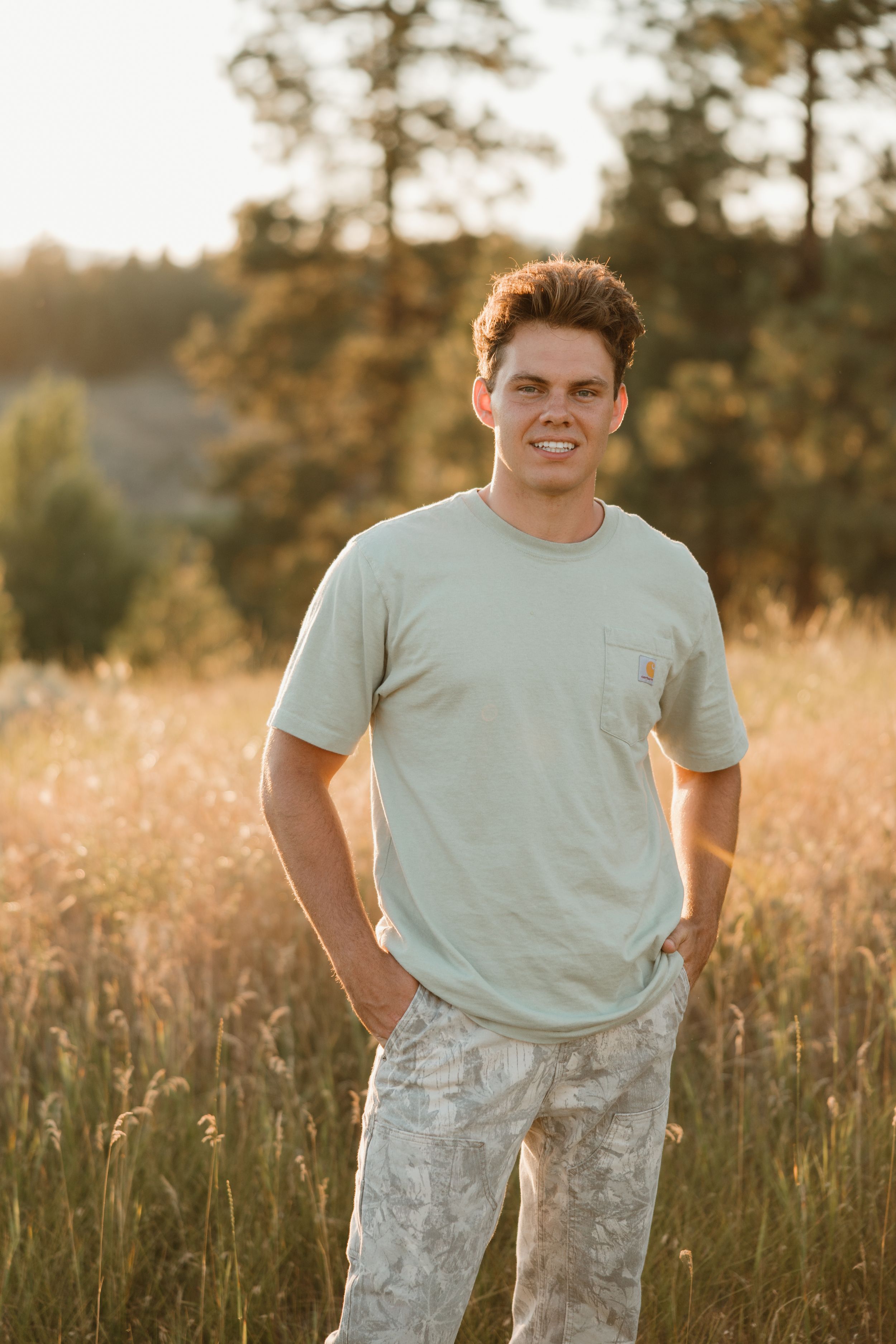 Military service member poses in front of tall grass field during golden hour sunset.