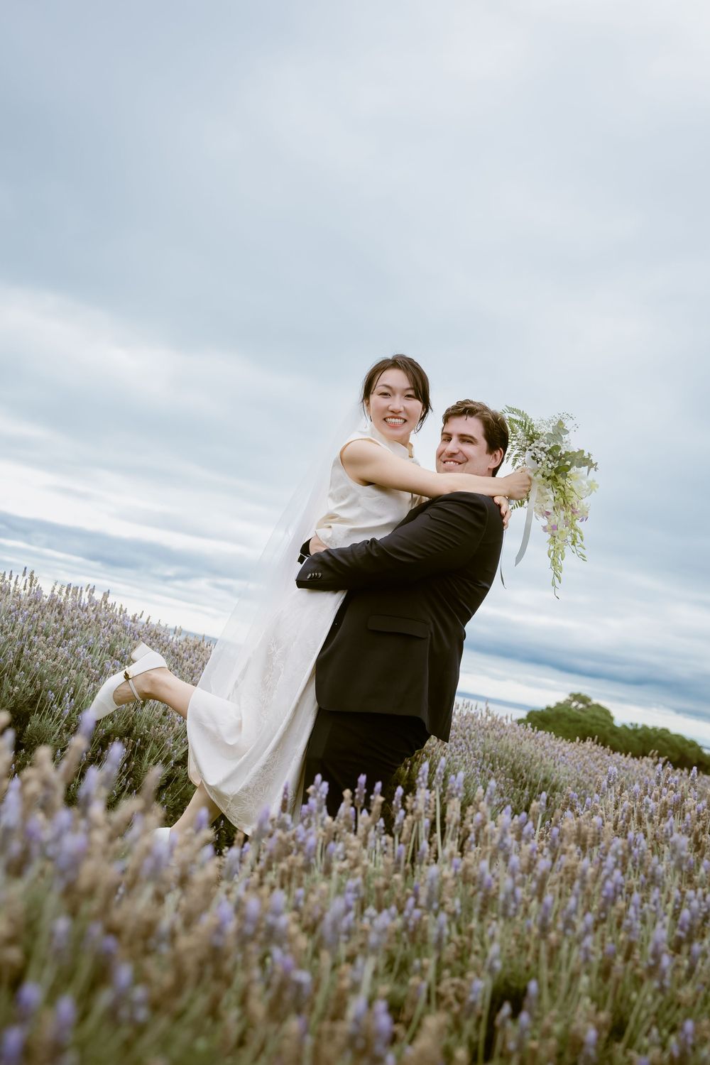 Romantic couple embraces in a blooming lavender field under cloudy skies.