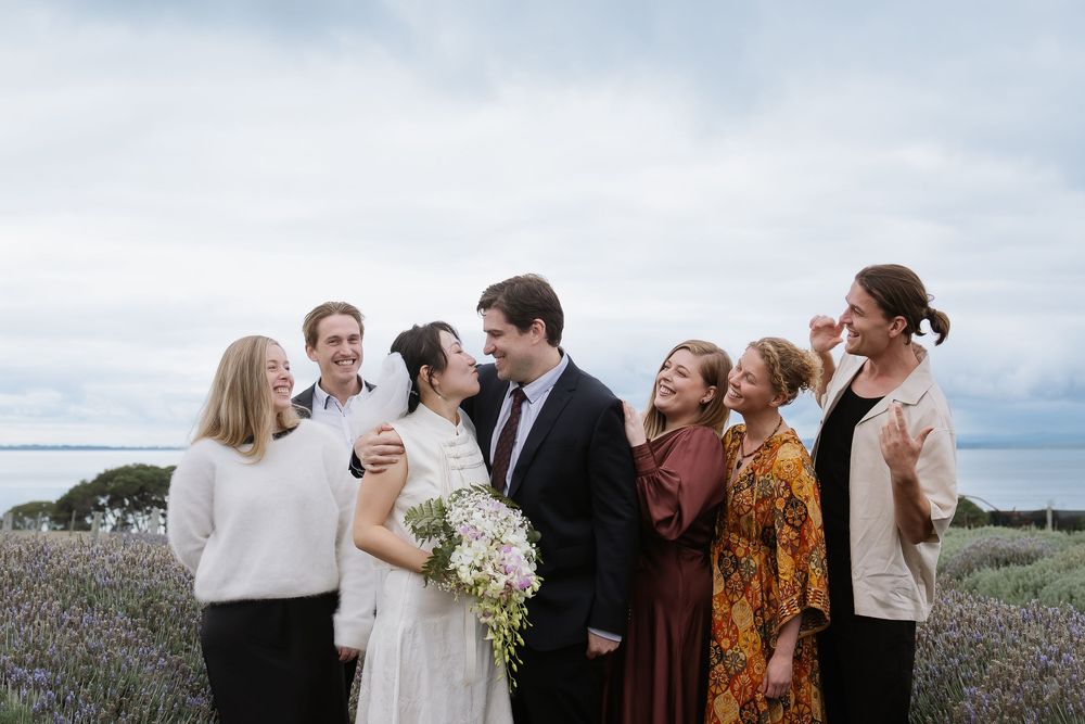 Wedding party celebrates joyfully together in an outdoor setting with bouquets and casual poses.