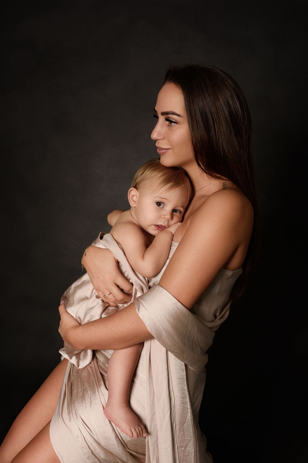 Intimate studio portrait of mom and her son showing gentle embraces in neutral tones against dark background.