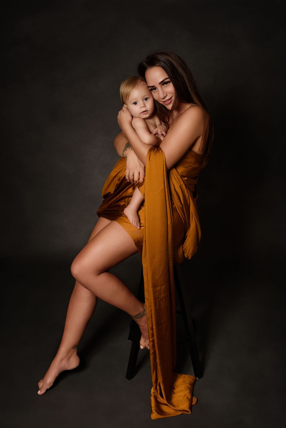 Artistic family portraits featuring warm rust-colored fabric and intimate pose of a mother and her son.