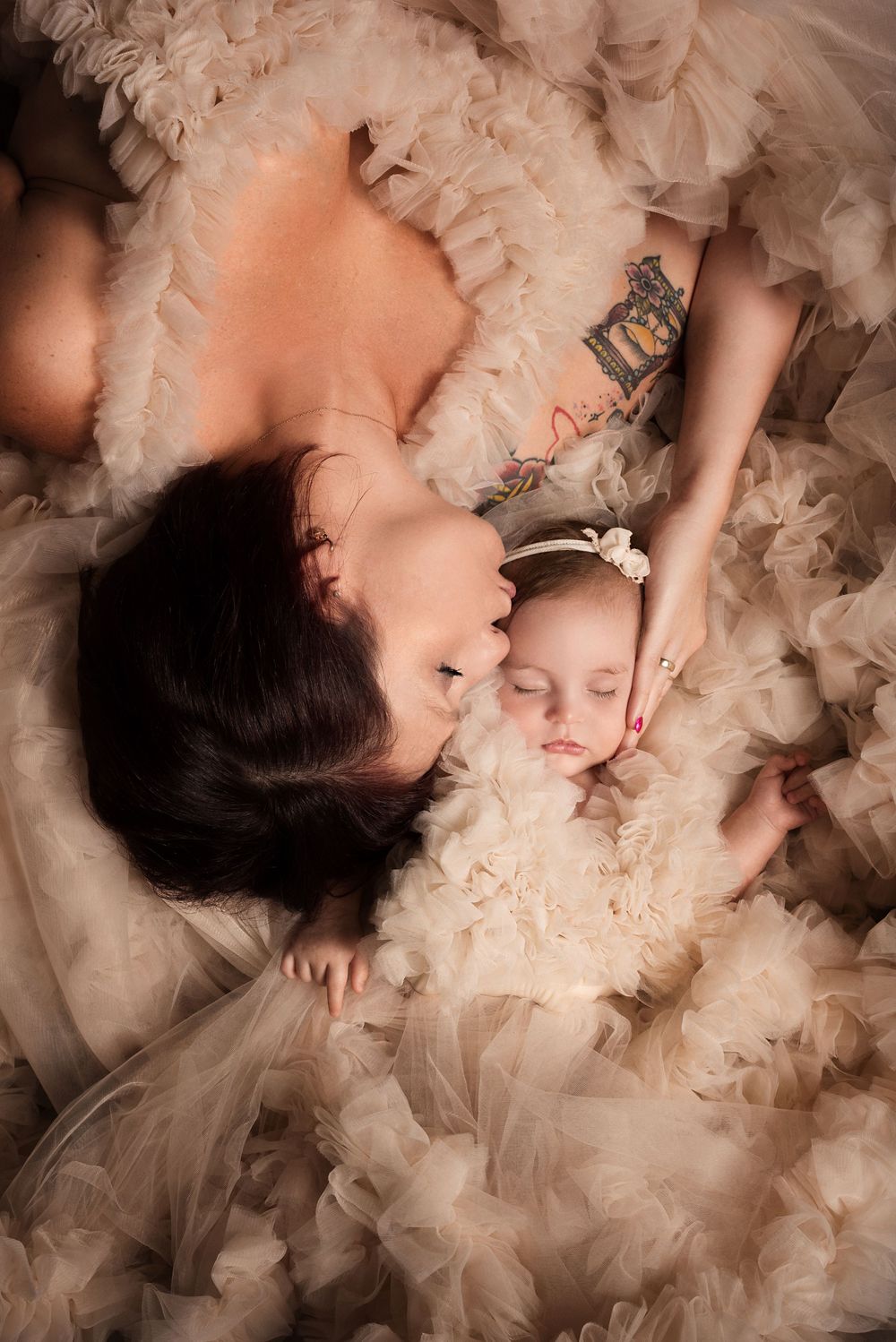 Overhead view of parent and child lying in soft tulle fabric creating ethereal effect.