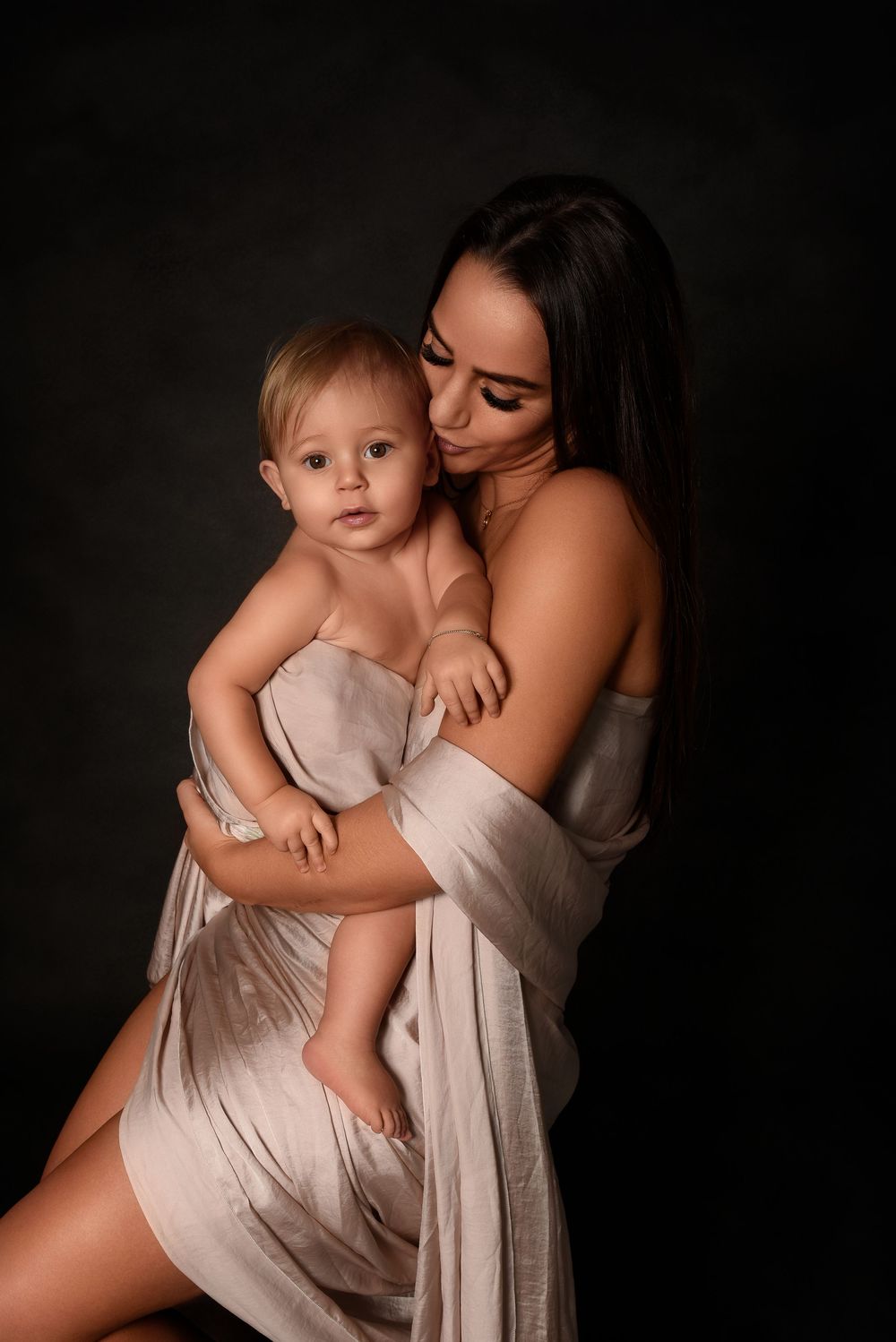 Tender studio portraits of parent and child in soft beige fabric against black backdrop.