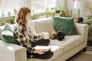 A cozy scene with someone in plaid reading on a white couch surrounded by houseplants.  Indoor Lifestyle Session Denton Texas