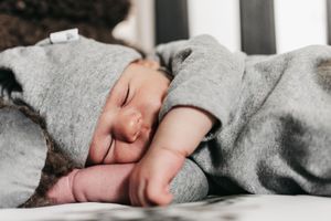 Sleeping baby in grey clothing curled up in white crib.  Indoor Newborn Session Arlington Texas