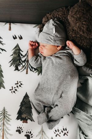 Baby napping in grey outfit on woodland-themed bedding with pine tree patterns.  Indoor Newborn Session Arlington Texas