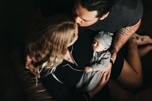 A tender family moment captured in moody lighting while leaning over a baby in gray clothing.  Indoor Newborn Session Arlington Texas