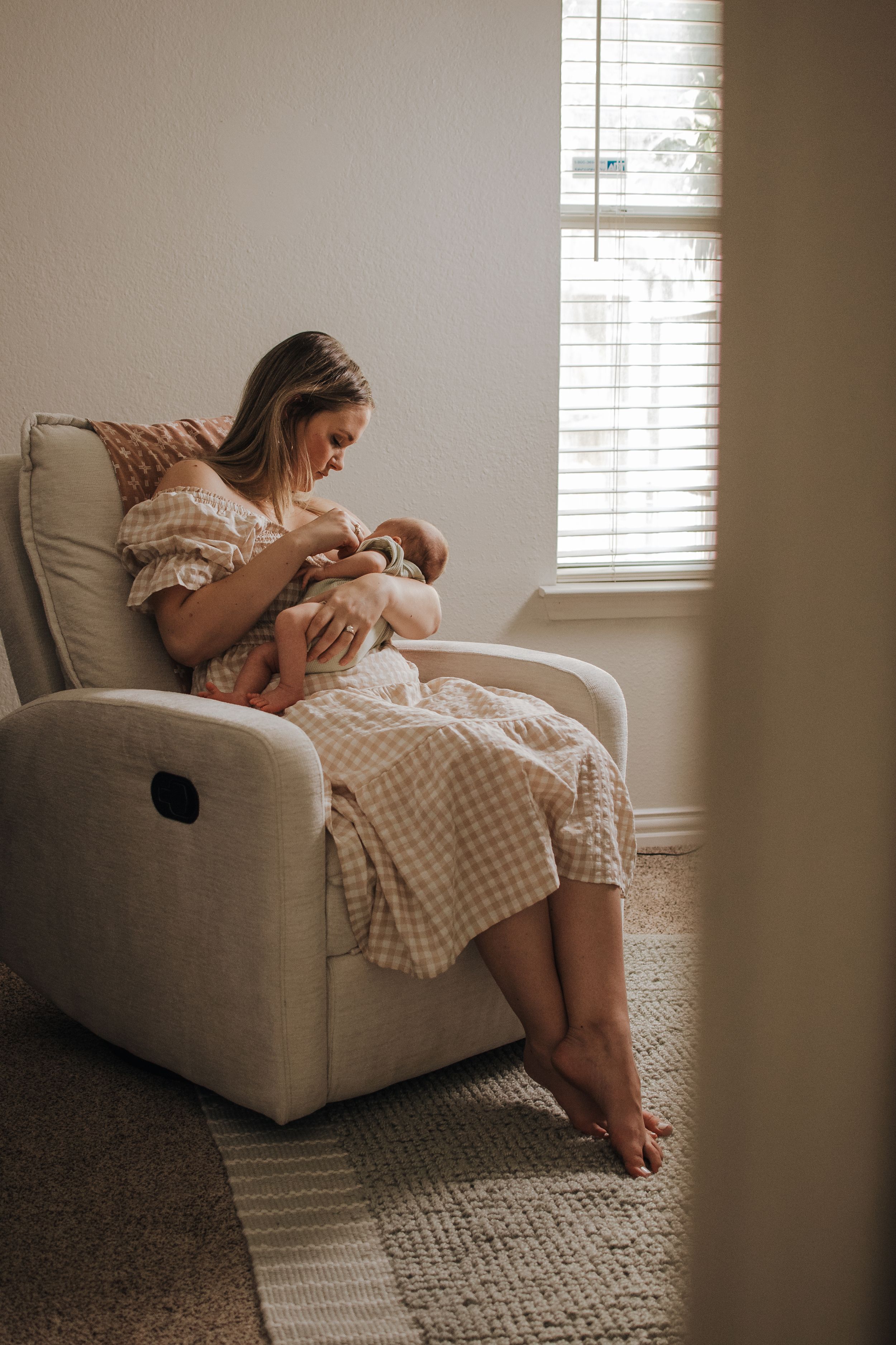 A tender moment in a recliner as parent bonds with newborn by window light. Indoor Newborn Session Saginaw Fort Worth Texas