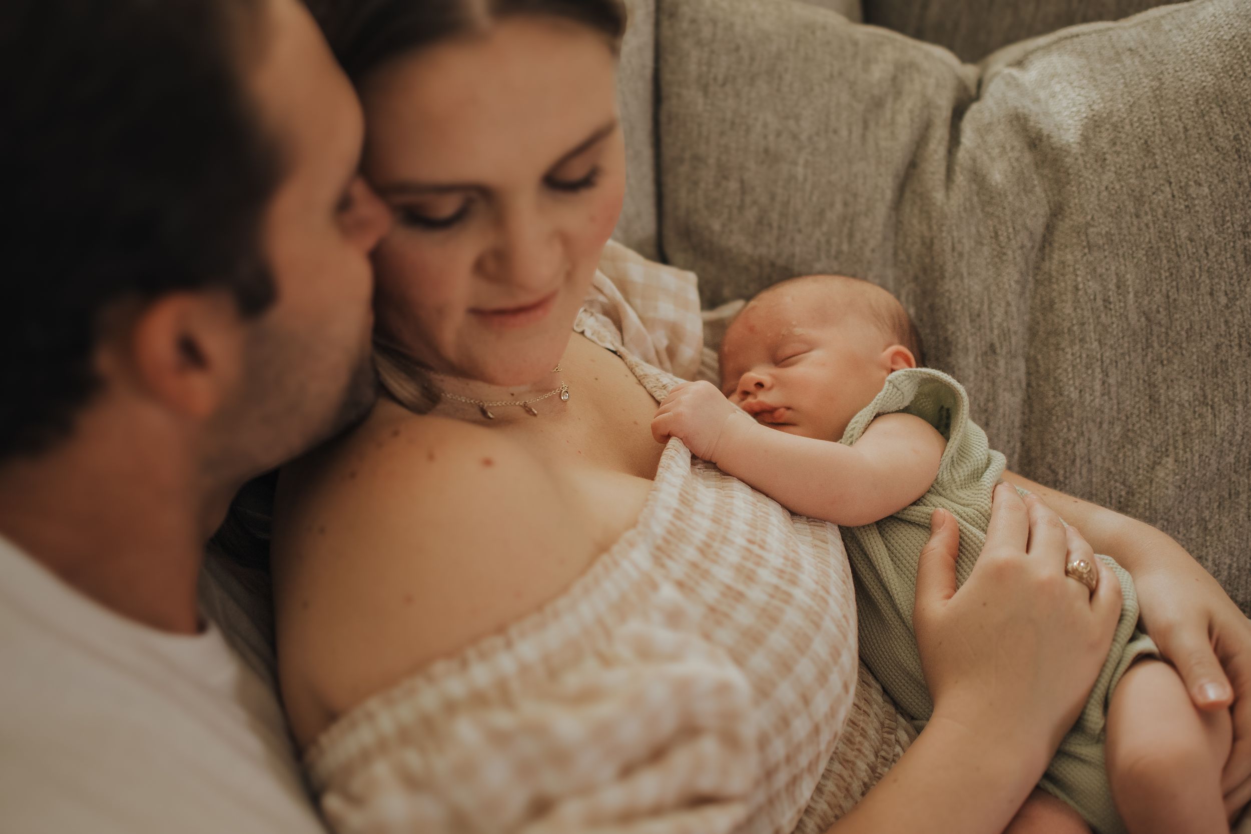 A peaceful family moment on the couch as parents cuddle with their sleeping newborn.  Indoor Newborn Session Saginaw Fort Worth Texas