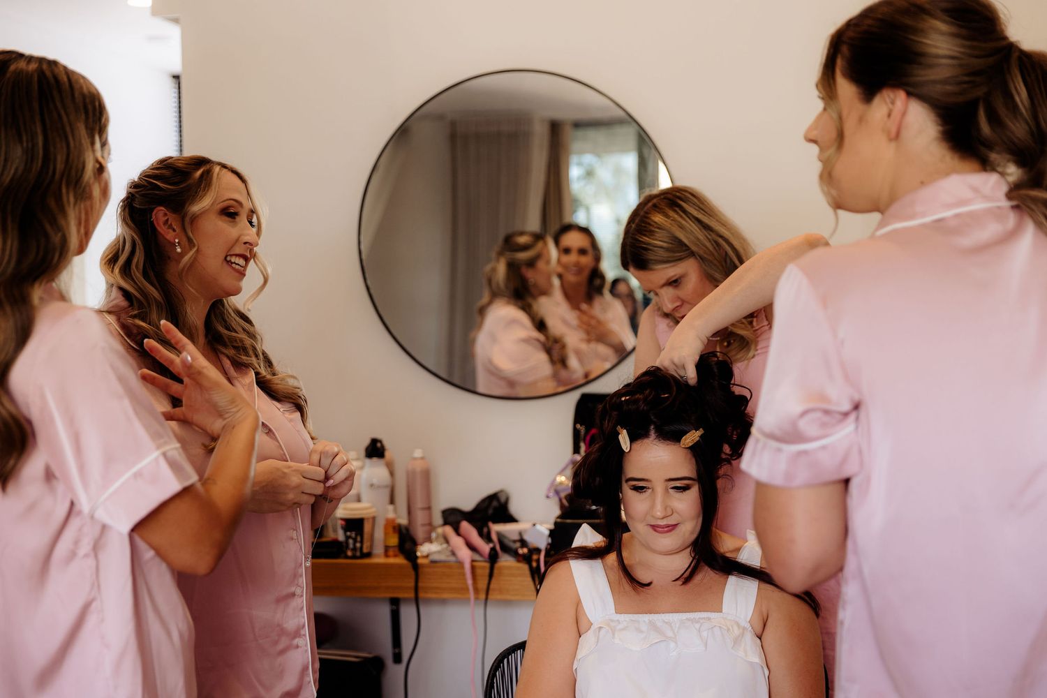 A series of candid moments between people getting ready in a pink-toned room with mirrors and various preparations underway.