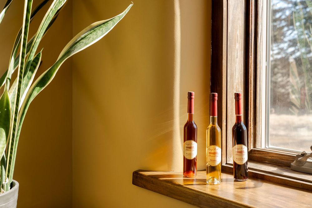 Three wine bottles displayed on wooden windowsill with houseplant and natural lighting.