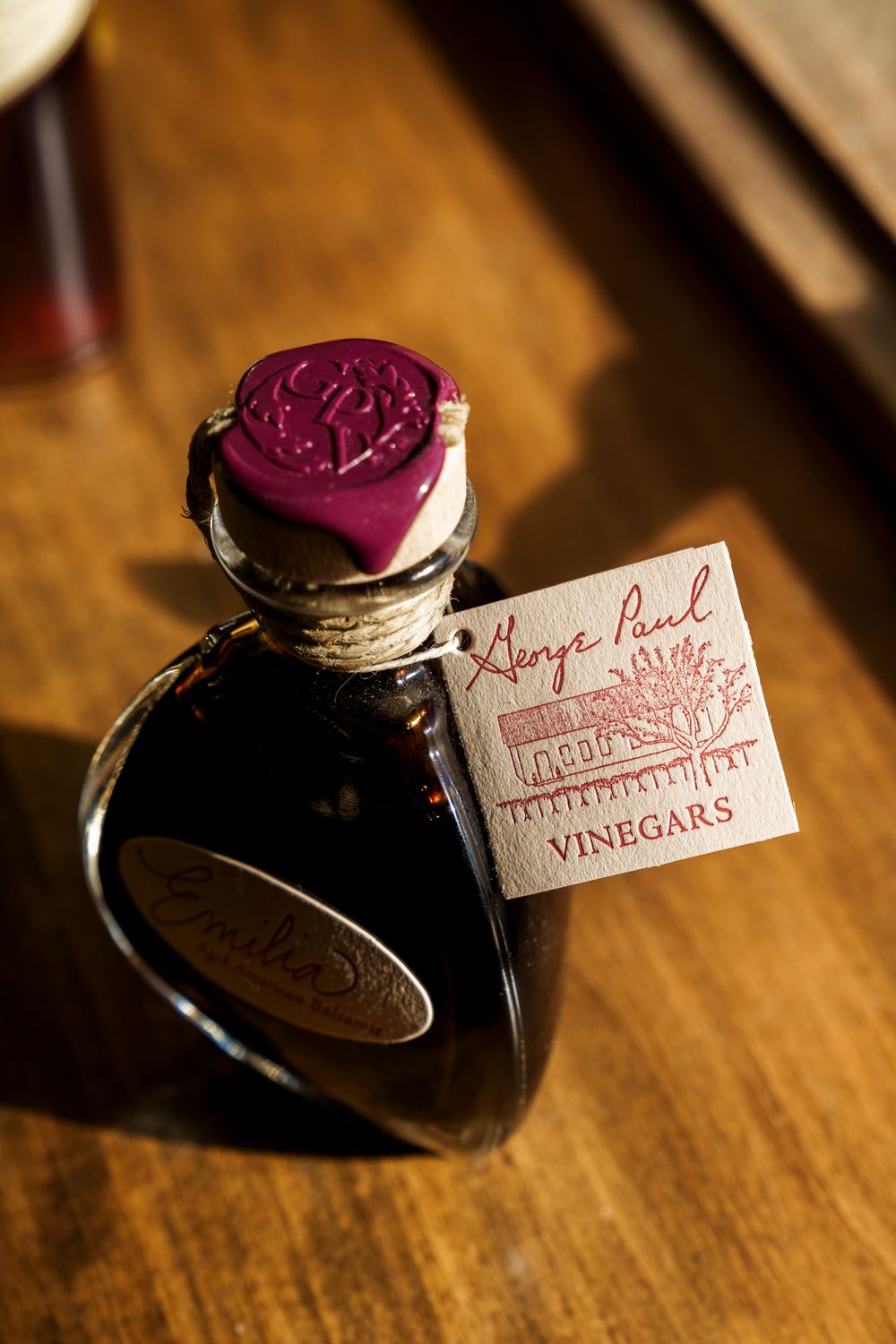 Ornate glass vinegar bottles with branded tags on wooden surface showing product detail.