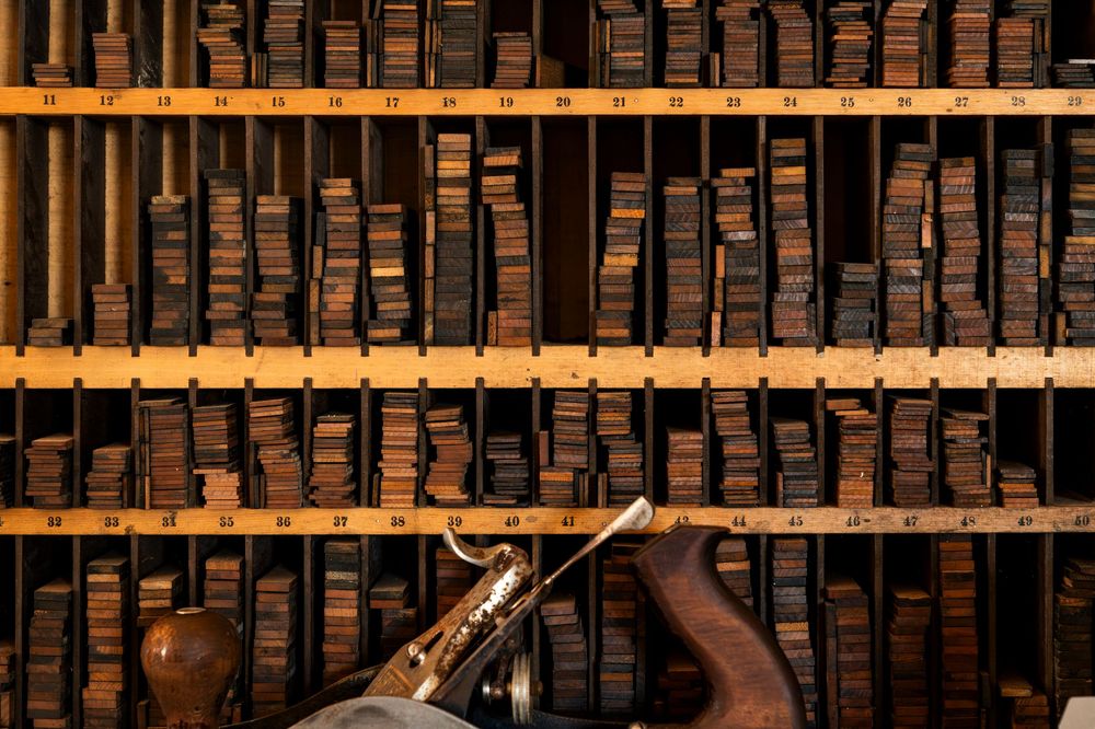 Rows of vintage wooden letterpress blocks arranged on wooden shelves.