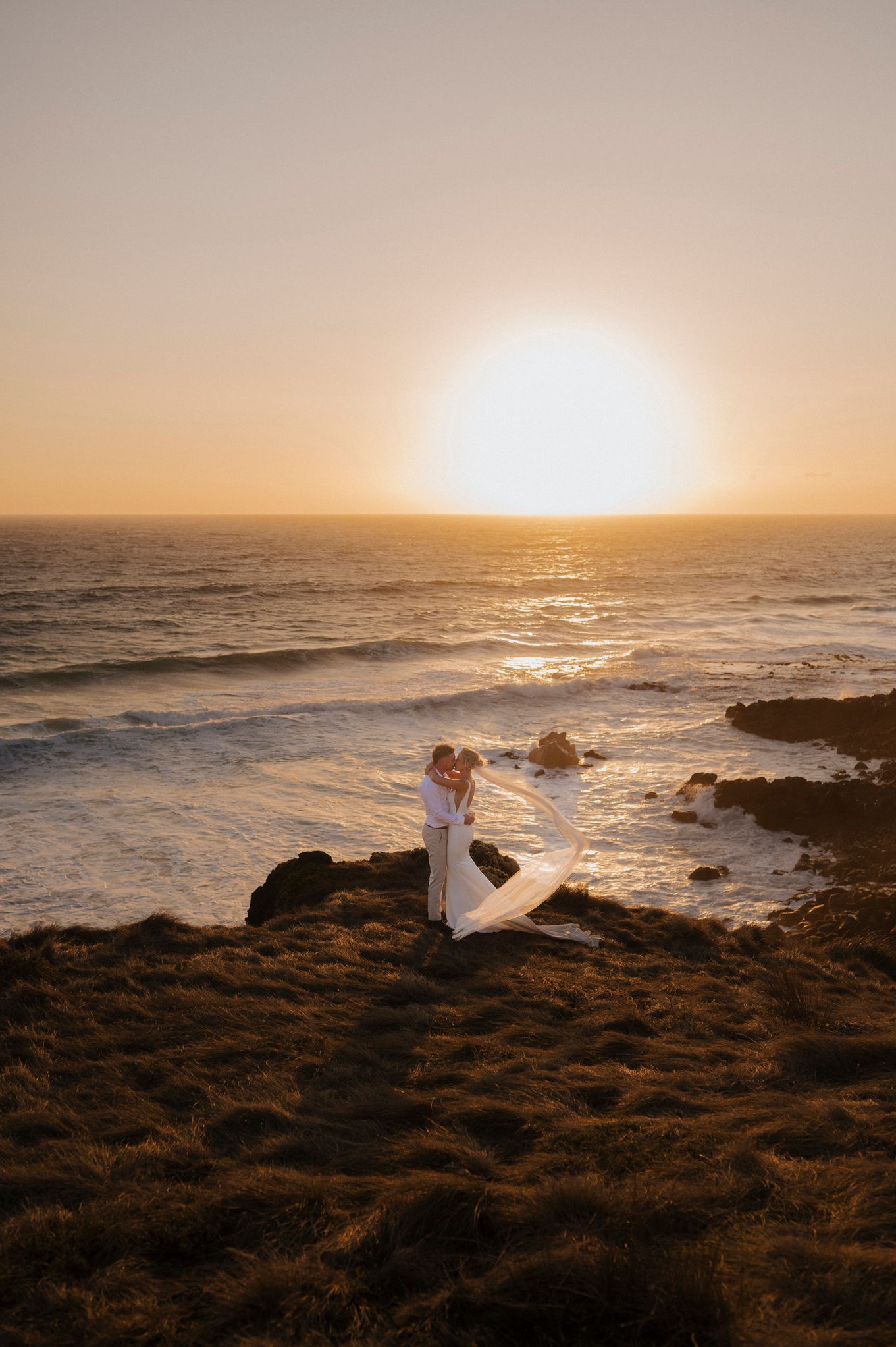 Golden hour wedding photos with the couple silhouetted against a stunning ocean sunset.