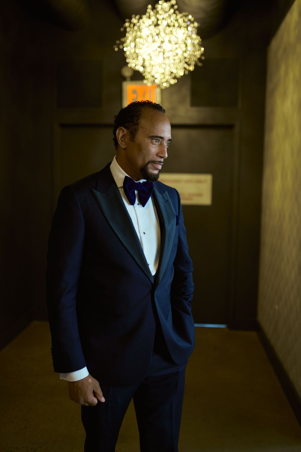 Dramatic portrait in dimly lit hallway with crystal chandelier overhead.