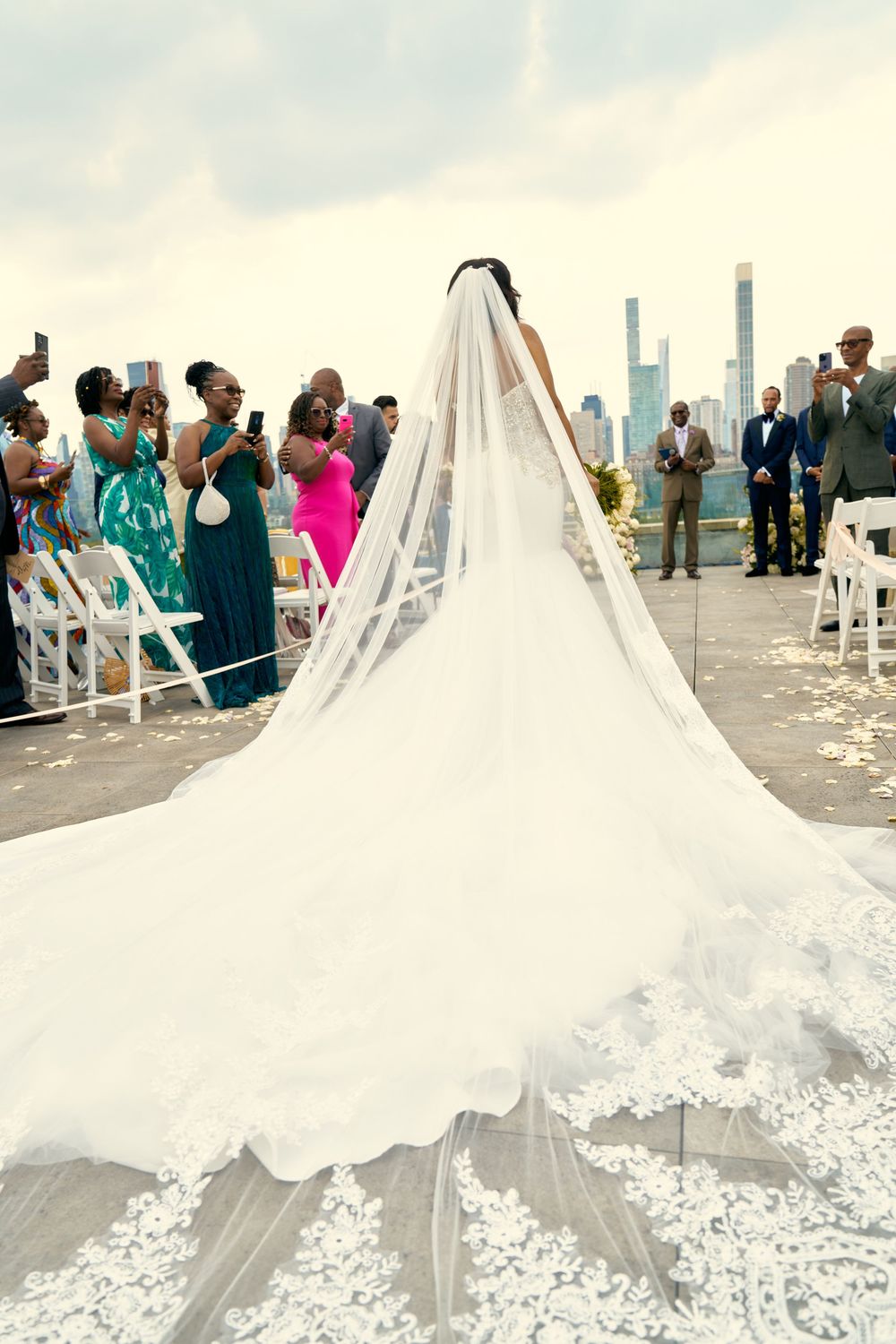 Outdoor rooftop wedding ceremony with flowing cathedral veil and city skyline backdrop.