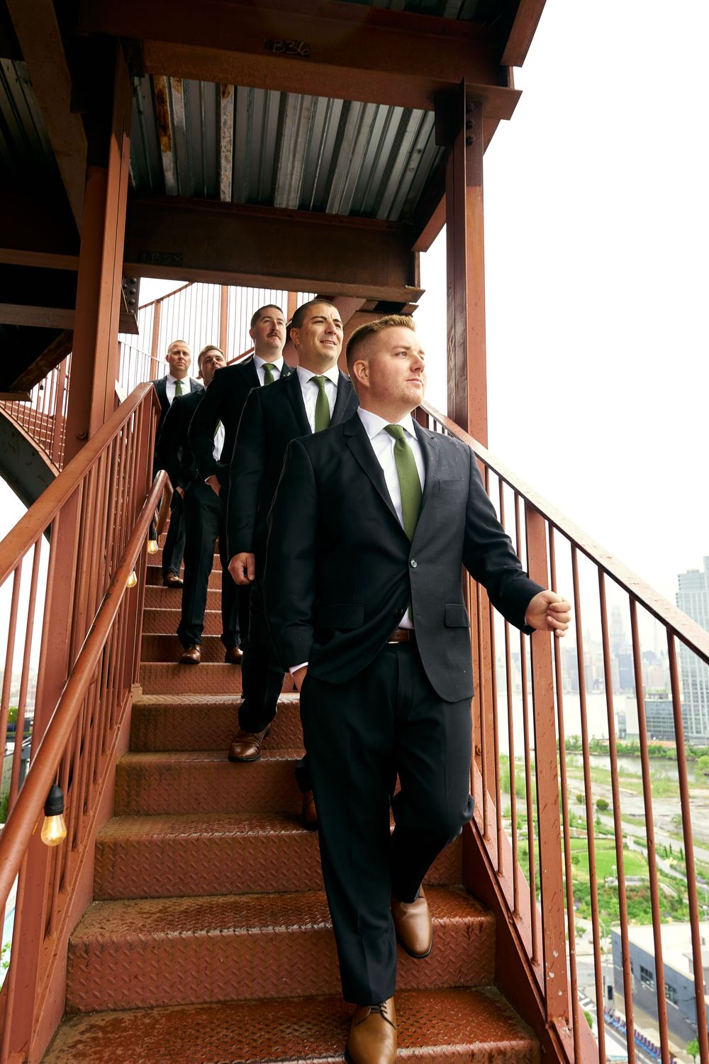 Groomsmen in dark suits descend rustic metal stairs in a wedding procession.
